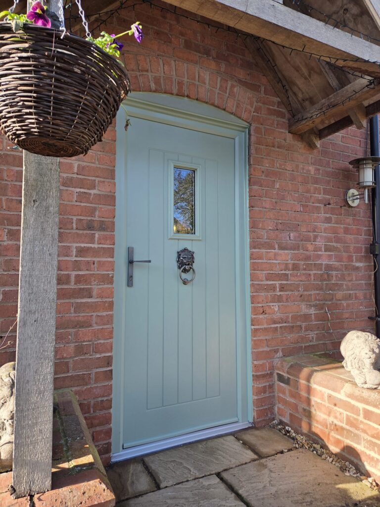 Sage green composite front door with lion knocker on brick house.