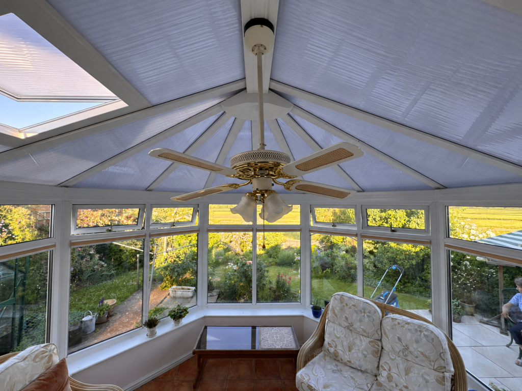 Bright conservatory interior with ceiling fan and garden view.