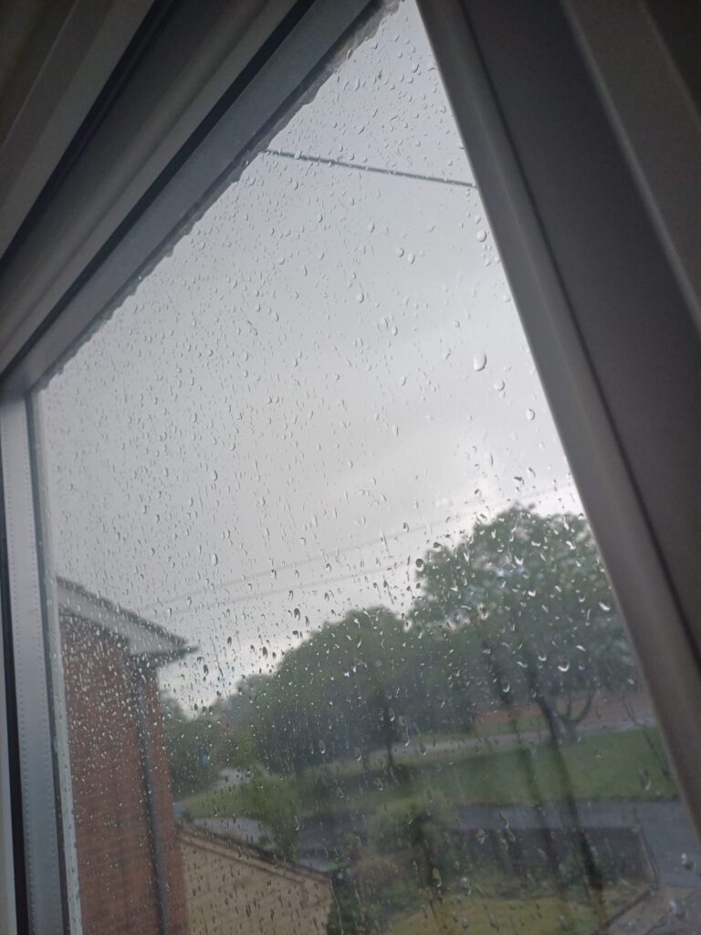 Raindrops cover a window pane, blurring the outdoor scene.