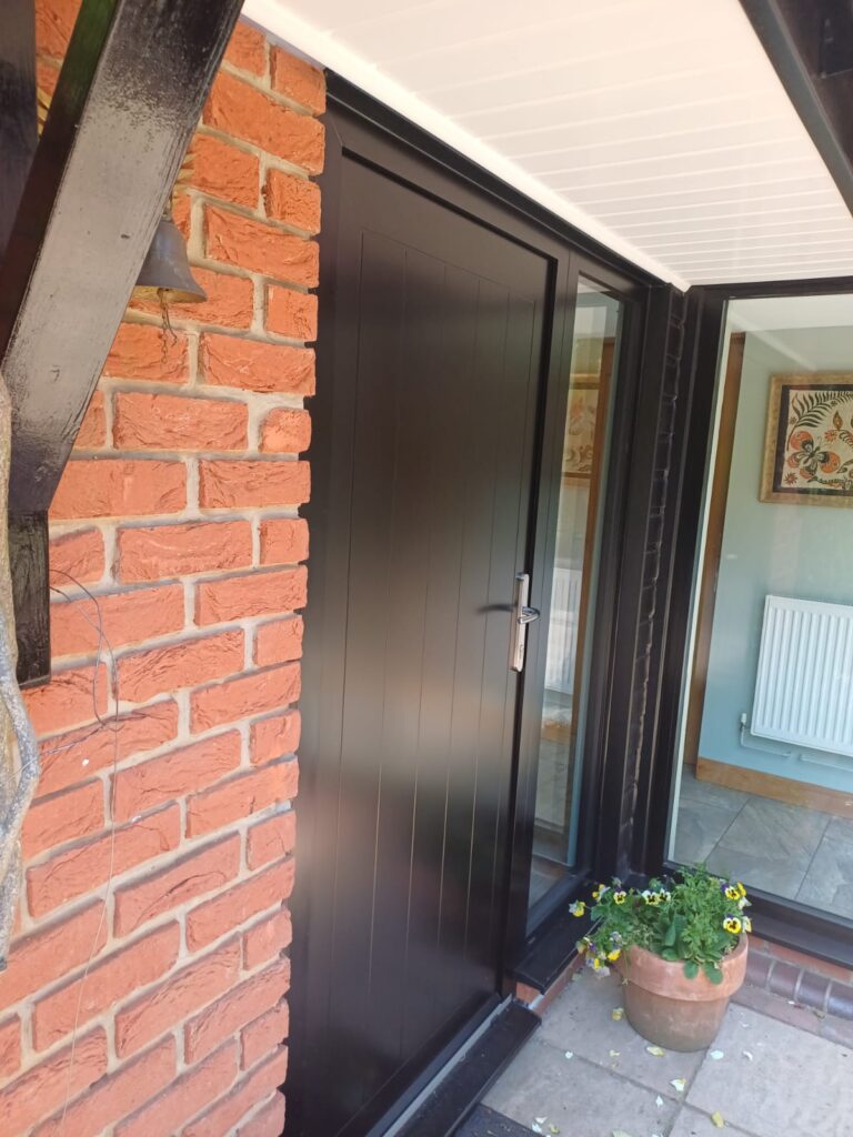Modern black front door, brick wall, pansies, and interior glimpse.