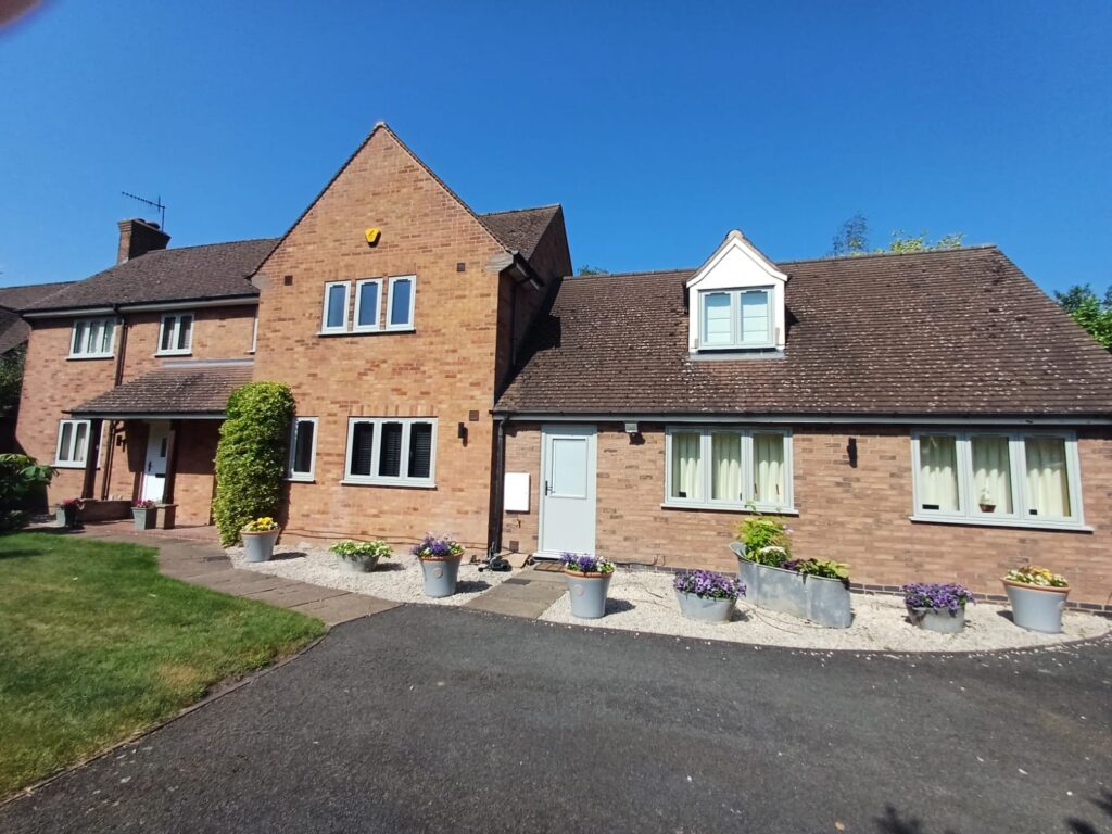 Large detached brick house with garden and potted flowers.